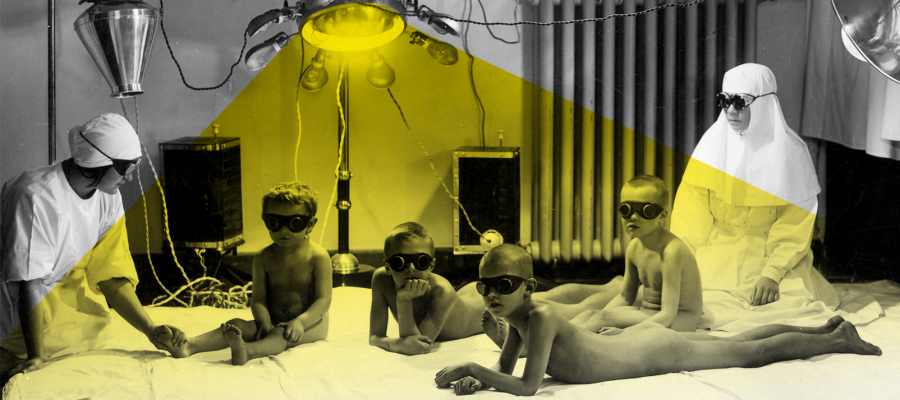 Кабинет врача, где на матрасе сидят две медсестры и четверо мальчиков в очках. Желтый свет сияет от лампы над ними.
