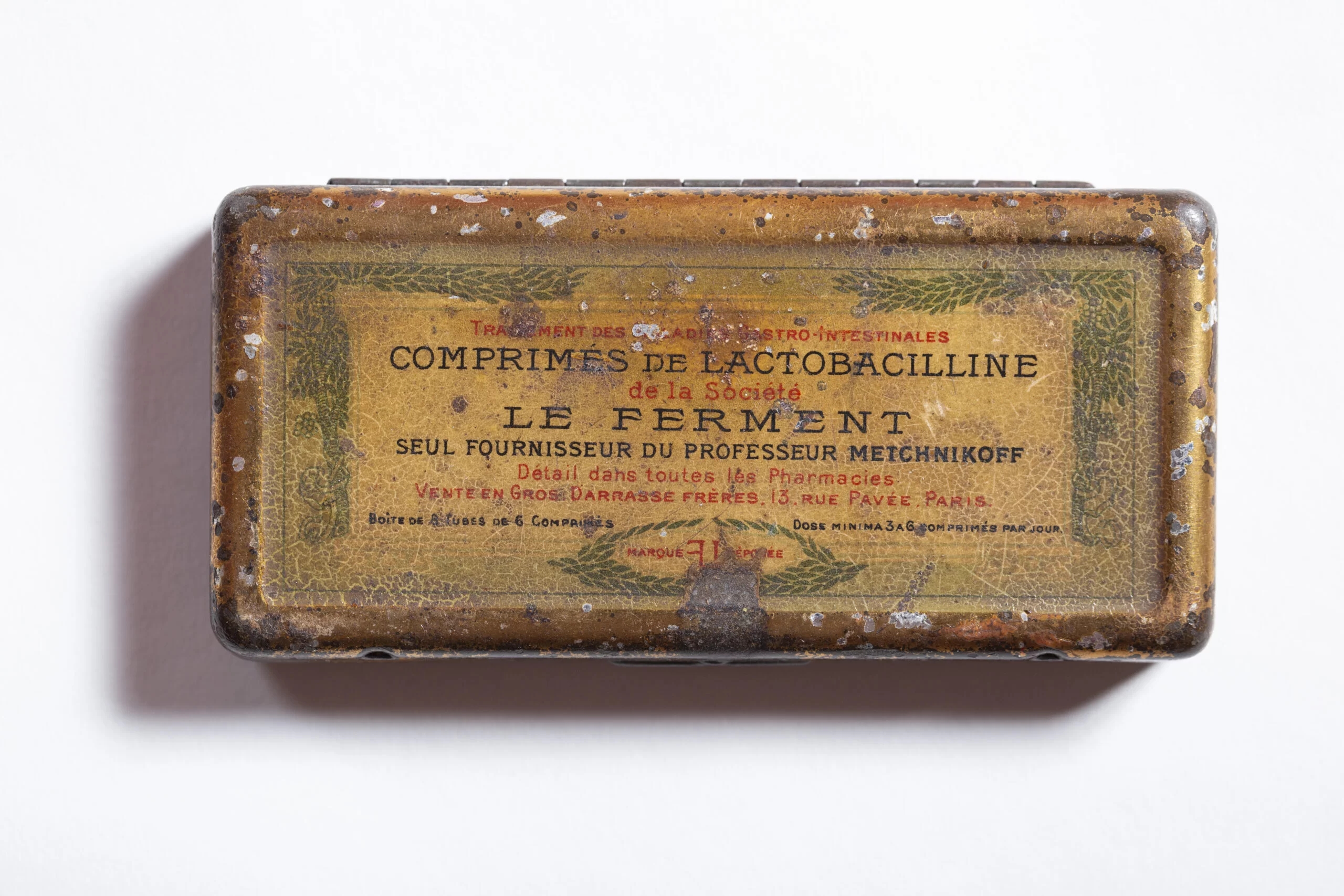 A brown, rectangular metal tin box with a tattered product information label on top.